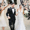 A bride and groom are walking through guests who are showering them with silk rose petals during their wedding exit.