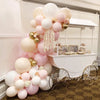 A large arrangement of pastel pink and white balloons decorated with gold accents for party use.