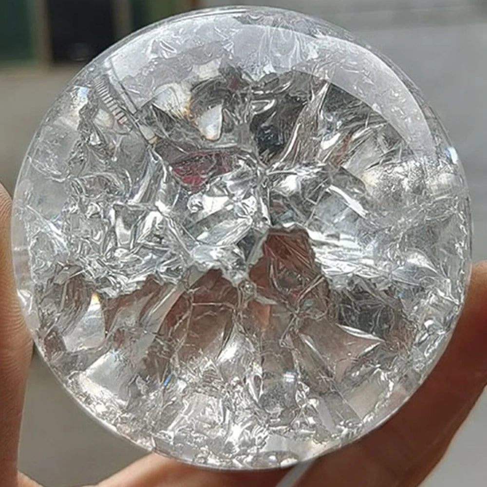 A clear crystal ball water feature ornament is held in a hand, showing its faceted surface.
