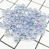 A pile of clear iridescent acrylic round beads for jewelry making scattered on a grid background.