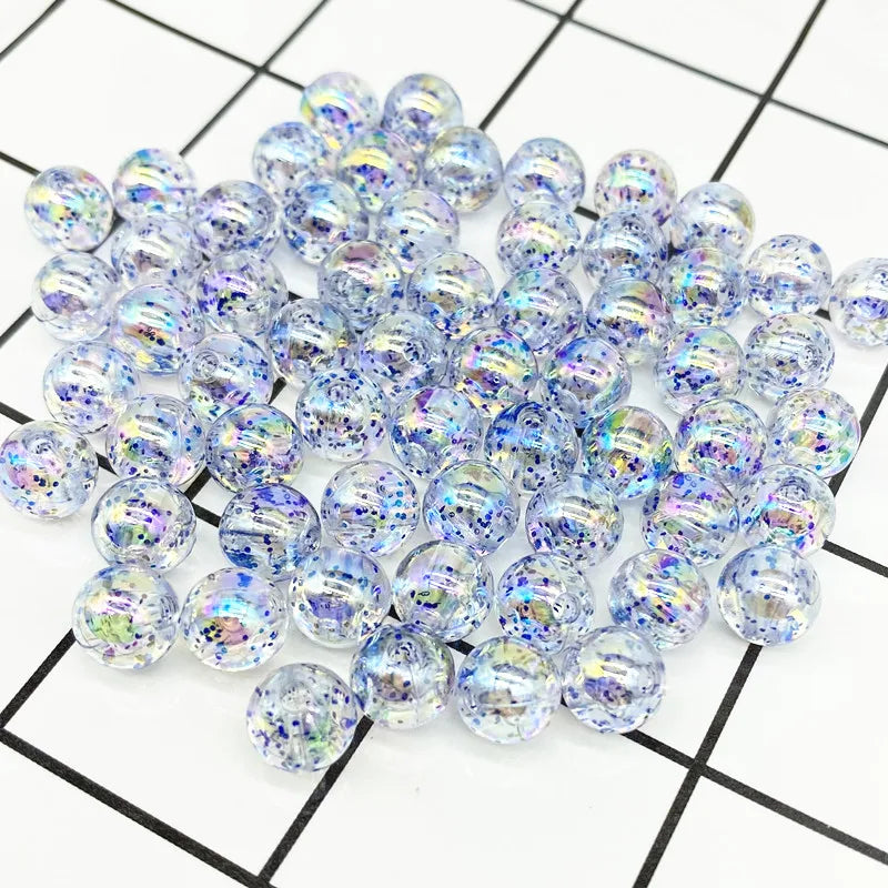 A pile of clear iridescent acrylic round beads for jewelry making scattered on a grid background.