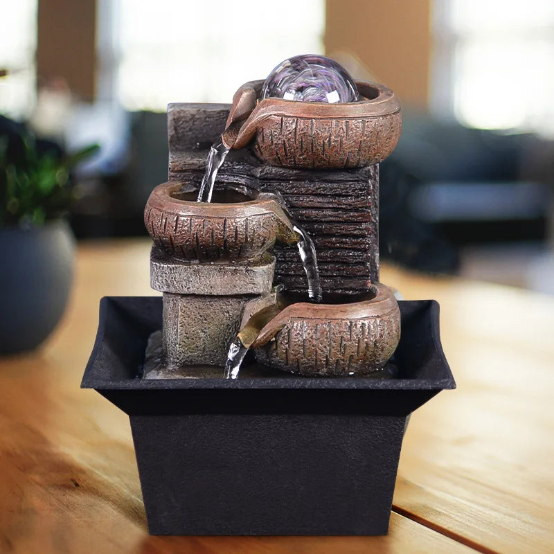A stacked, rustic brown tabletop water fountain with a clear sphere at the top, set on a dark square dish.