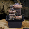 A tabletop water fountain featuring stacked, rustic brown ceramic pots with flowing water and a clear glass orb.