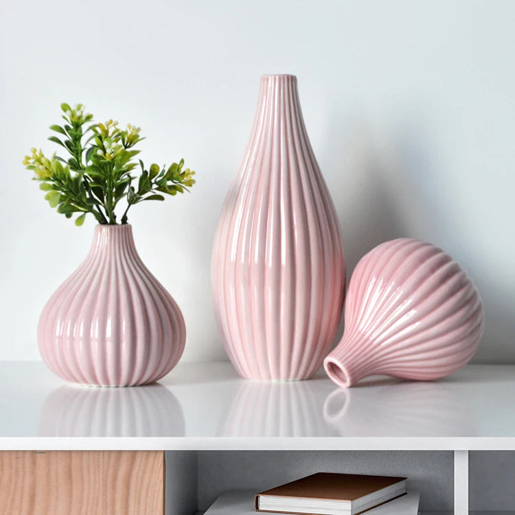 A pink ceramic flower vase with vertical ridges and a matching spherical vase on a white table.