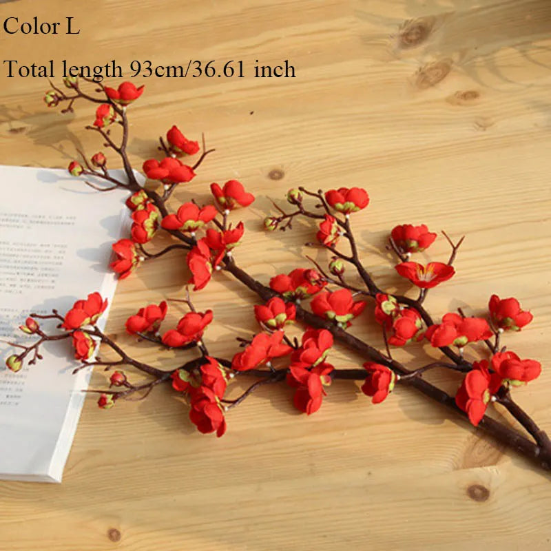 Red artificial silk cherry blossom branches with small red flowers on a wooden surface.