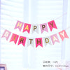 Decoración de una pancarta con banderines rosas y blancos que deletrean 'Feliz Cumpleaños' en un ambiente claro y brillante.