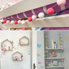 A colorful felt ball garland featuring pink, white, and red spheres displayed on a shelf.