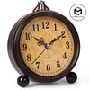 A vintage metal battery alarm clock with a round face and Roman numerals, sitting on a surface.