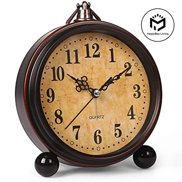 A vintage metal battery alarm clock with a round face and Roman numerals, sitting on a surface.