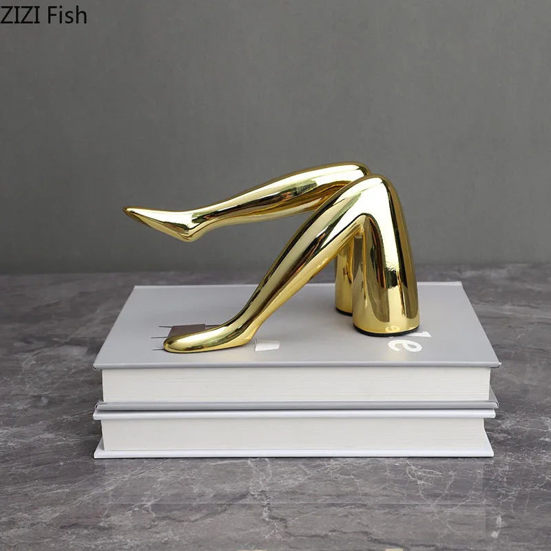 A gold faux finish human body resin art sculpture shaped like a leg resting on a stack of white books.