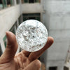 A hand holds a clear, spherical crystal ball water feature ornament against a blurred architectural background.