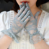 A pair of light blue sheer lace gloves worn by a woman, featuring delicate floral patterns.