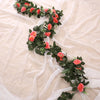 A green silk rose hanging vine garland with pink and orange roses laid on sheer white fabric.