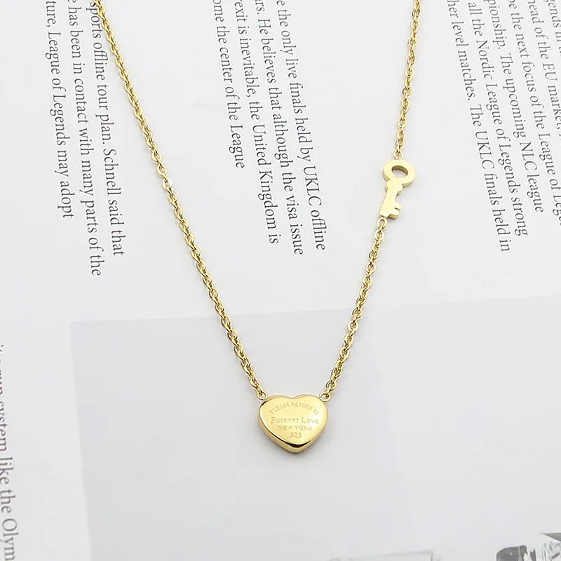 A gold-colored titanium steel heart lock key pendant necklace with a chain and a charm.
