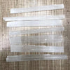 A collection of thin, translucent white selenite crystal wands laid diagonally on a wooden surface.