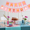 Decoración de pancarta de cumpleaños rosa y dorado colgando sobre una mesa con flores y dulces.