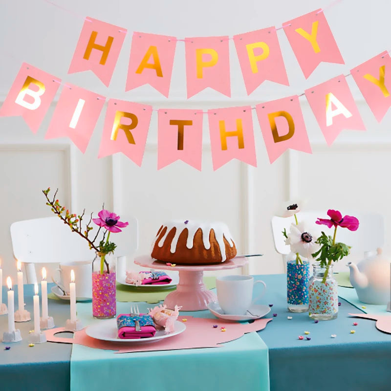 Decoración de pancarta de cumpleaños rosa y dorado colgando sobre una mesa con flores y dulces.