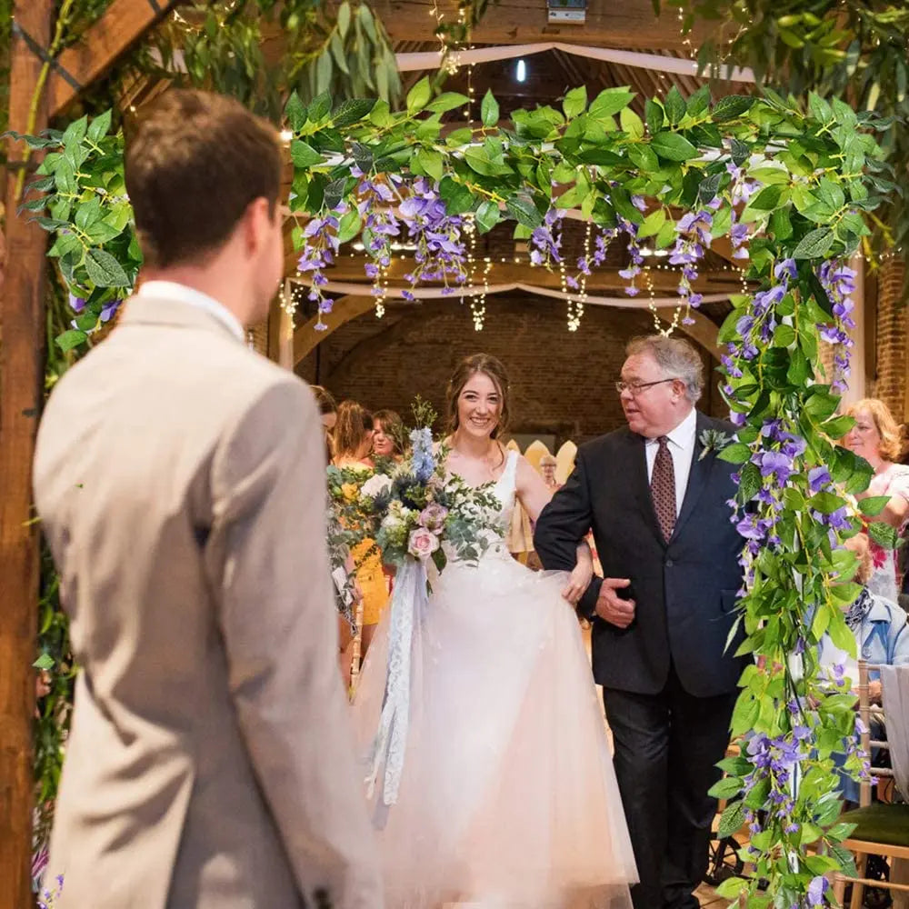 A bride and groom stand under a lush silk wisteria garland vine for a wedding ceremony.