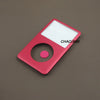 Pièce de face rouge et blanche pour kit de réparation iPod Classic posée sur une surface marron.