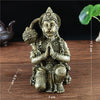 Bronze Hanuman statue figurine with hands folded in prayer sitting on a wooden surface.