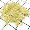 A pile of clear yellow and gold acrylic round beads for jewelry making laid on a grid background.