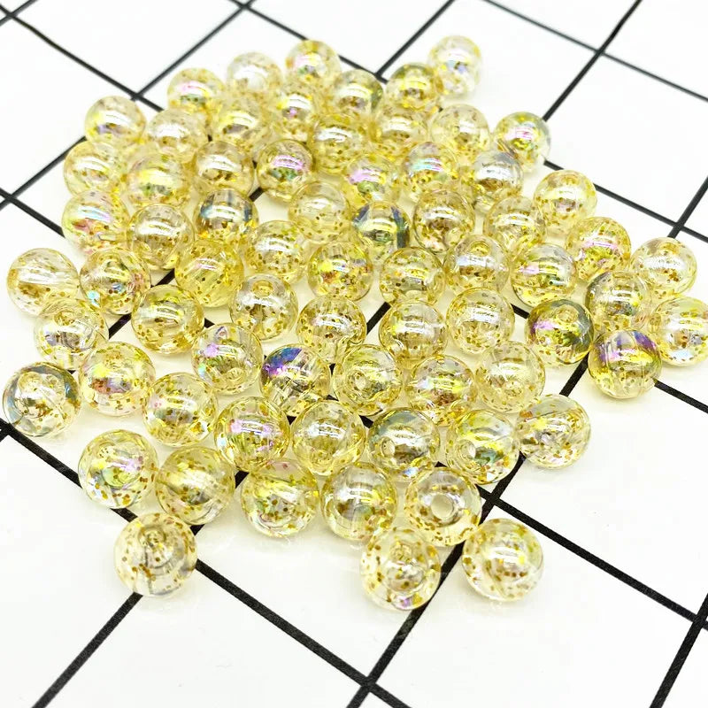 A pile of clear yellow and gold acrylic round beads for jewelry making laid on a grid background.