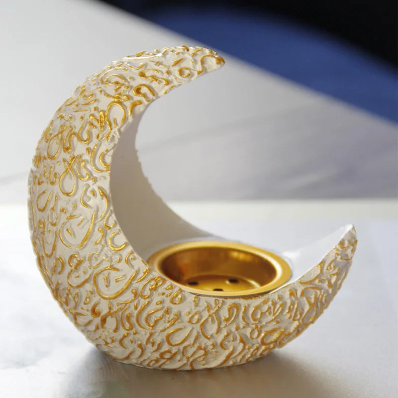 An antique crescent shaped resin incense burner with gold detailing sits on a white surface.