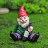 A miniature resin gnome statue with a red hat and white beard sitting in green grass.