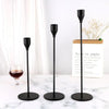 A set of three black iron candle holders with tall slender stems displayed on a white marble surface.