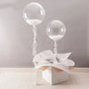 Clear bobo balloons with white filling tied on strings displayed on a white box