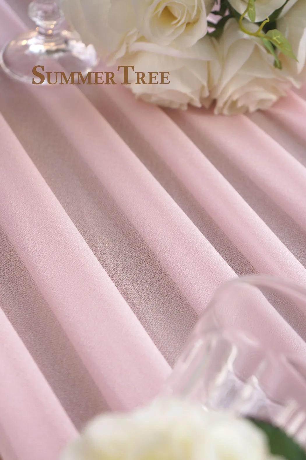 Soft pink sheer chiffon fabric draped in vertical pleats with white roses in the background