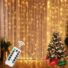 Warm white LED curtain lights with remote control illuminating a Christmas tree and gift box.