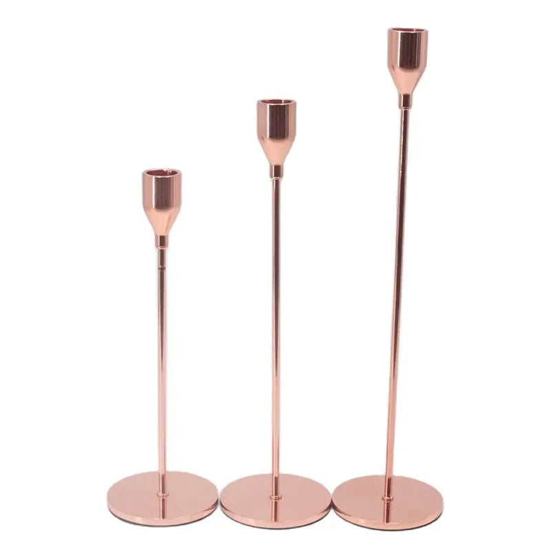 A set of three rose gold iron candle holders with tall slender stems.