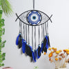 Handmade boho evil eye dream catcher wall decor with a black mesh and blue feathers hanging against a white wall.