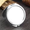 A silver mini double-sided folding makeup mirror with a hinged case resting on a dark wooden surface.