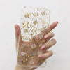 A hand holds a clear resin mold embedded with shiny gold foil flakes for art and jewelry making.