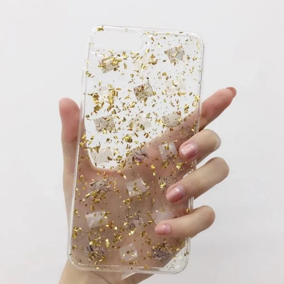 A hand holds a clear resin mold embedded with shiny gold foil flakes for art and jewelry making.