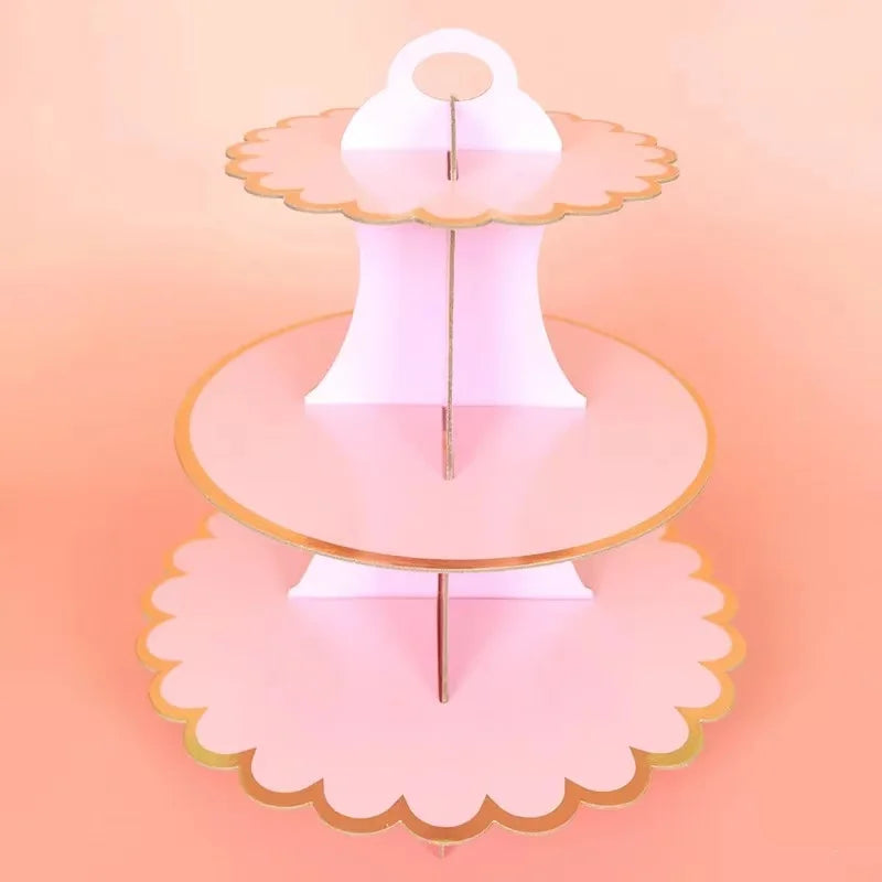 A pink cardboard cupcake stand with three tiers, featuring scalloped edges and a gold rim.