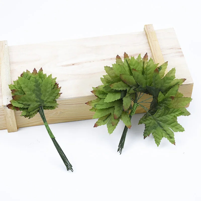 A set of twelve silk leaf artificial plant stems with vases displayed on a light wooden surface.