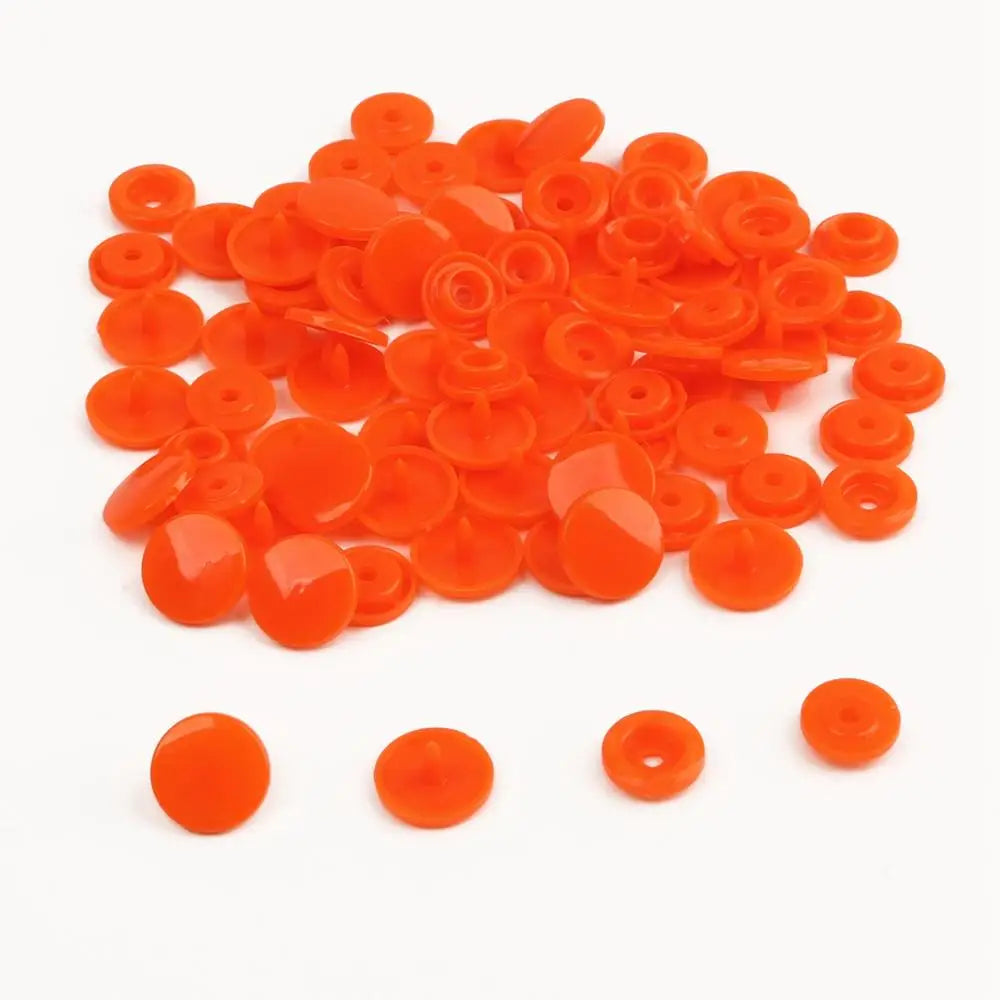 A pile of assorted bright orange snap buttons, measuring 12mm and 10.5mm, for crafting.
