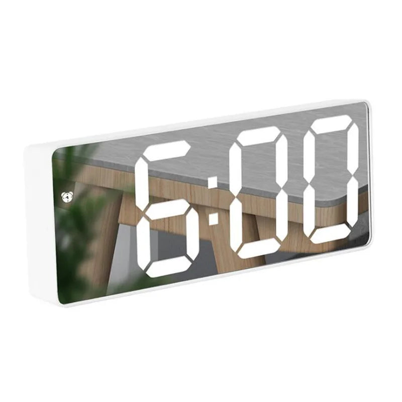 A digital alarm clock displaying 6:00 on a white panel with a wooden background.