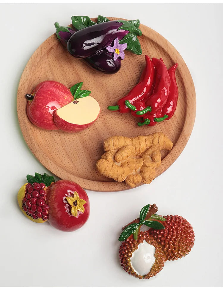 A set of realistic fruit and vegetable fridge magnets including a plum, apple, chili peppers, and a raspberry on a wooden boa