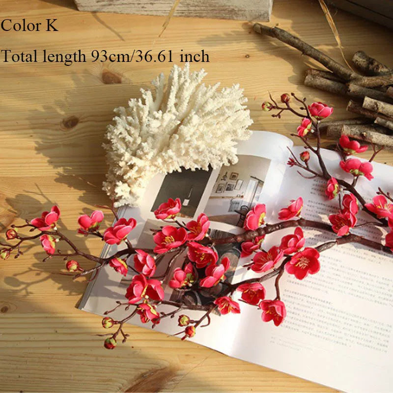 Artificial silk cherry blossom branches with pink flowers and a white fluffy element displayed on a wooden surface.