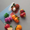 A set of realistic, colorful fruit and vegetable fridge magnets including a pomegranate, citrus fruit, and various colorful p