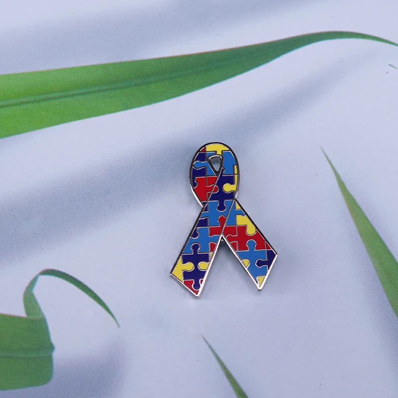 A puzzle ribbon brooch pin featuring the colors of the autism awareness rainbow
