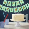 Un pastel de cumpleaños blanco decorado con banderas doradas y palitos de colores sobre una mesa.
