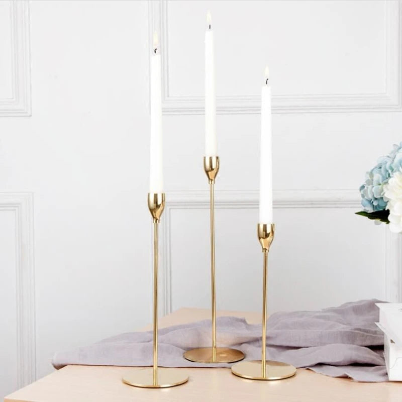 Three tall gold iron candles in a decorative holder on a light surface.