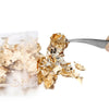 A pair of tweezers is lifting shiny gold foil flakes from a clear plastic bag for resin art or jewelry making.
