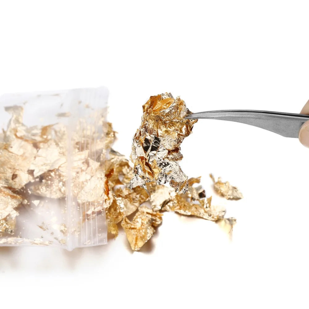 A pair of tweezers is lifting shiny gold foil flakes from a clear plastic bag for resin art or jewelry making.