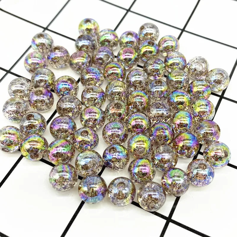 A pile of 50 clear and iridescent acrylic round beads for jewelry making scattered on a black and white grid.